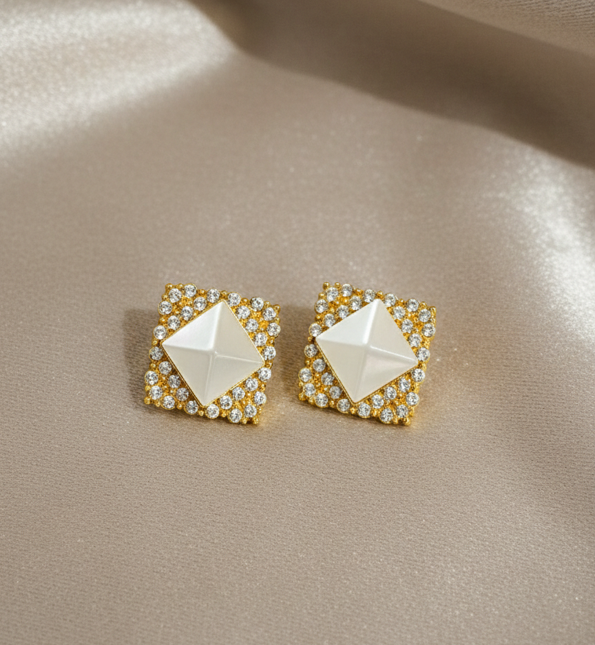 Pair of gold and white earrings on a beige fabric background